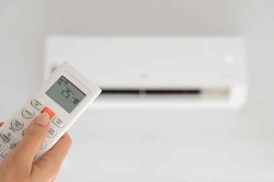 Woman Hand Holding Remote Controller Directed On The Air Conditioner Inside The Room