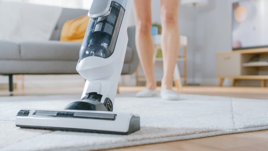 Woman In Jeans Shirt And Shorts Vacuum Cleaning A Carpet