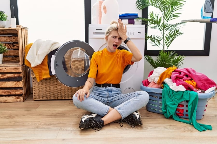 Young Blonde Woman Doing Laundry Sitting By Washing Machine