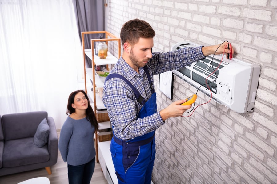 Young Woman Looking At Technician Examining Air Conditioner With Digital Multimeter