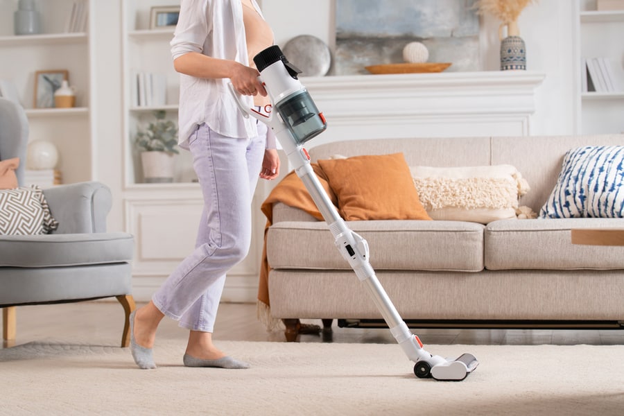 Young Woman Uses Cordless Vacuum Cleaner To Clean Home Carpet