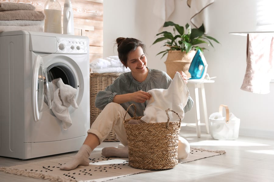 Young Woman With Laundry Basket Near Washing Machine At Home